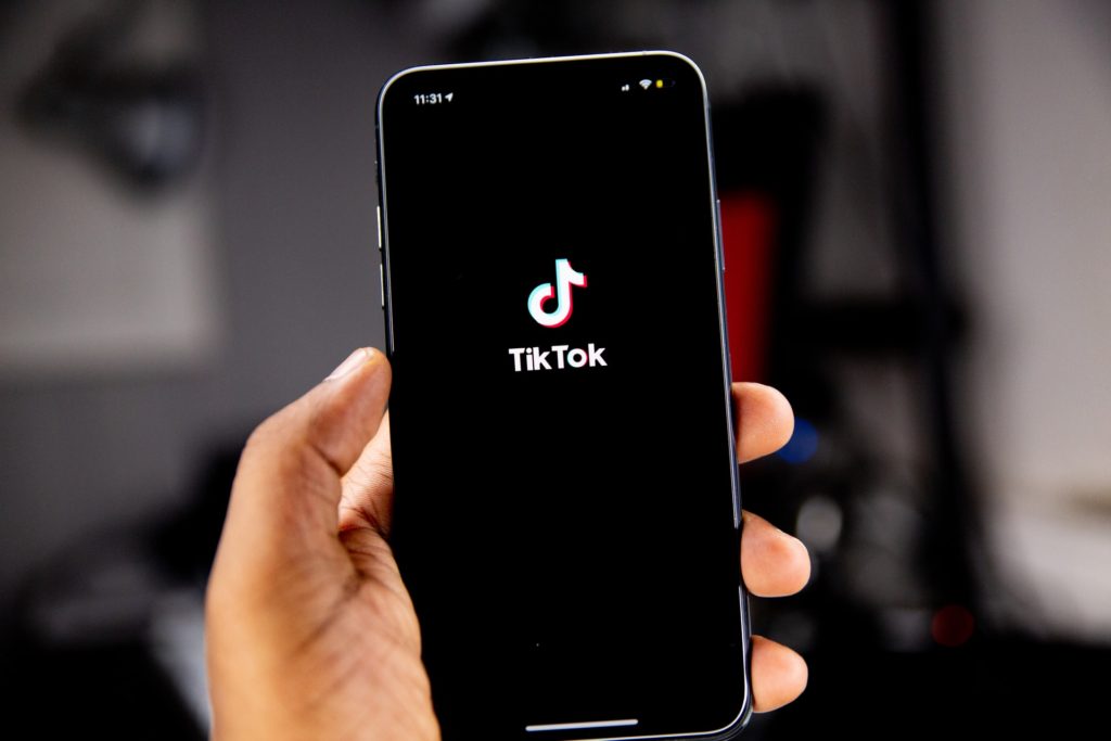 A smartphone in a child's hand with the TikTok app opening up on the screen.