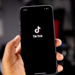 A smartphone in a child's hand with the TikTok app opening up on the screen.