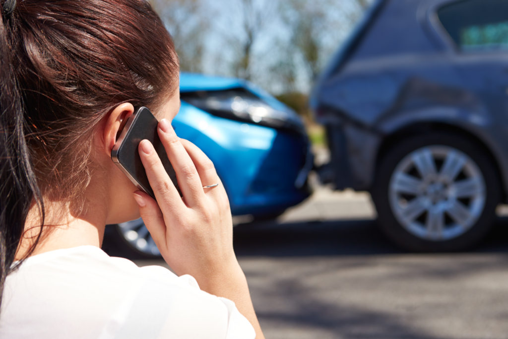 A woman on her cell phone at the scene of her car accident.