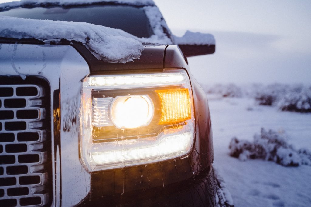 Black pickup truck with headlights turned on and parked on a snowy path.