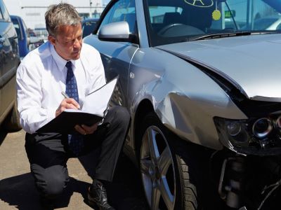 An insurance adjuster investigating accident damage on a vehicle.