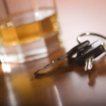 A set of car keys in the foreground and glass of whiskey behind.