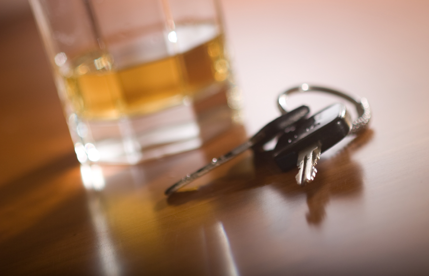 A set of car keys in the foreground and glass of whiskey behind.