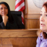 Woman sits and testifies in a courtroom with a judge present.