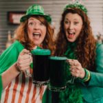 Two women celebrate St. Patrick's day with green beer.