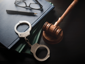 Handcuffs, a gavel, glasses and a pen on a desk.