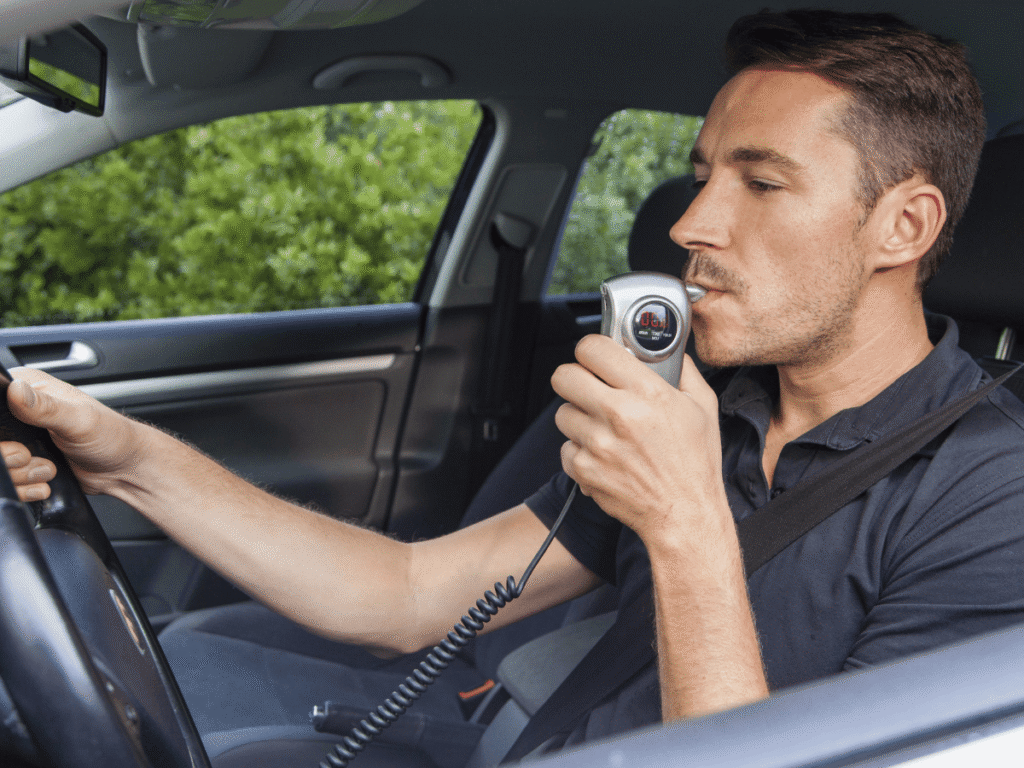 A man in the drivers seat taking a breathalyzer