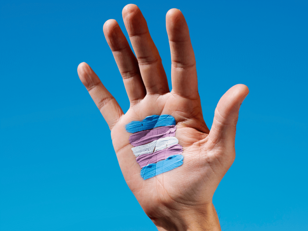 Hand with transgender flag painted on palm against blue sky