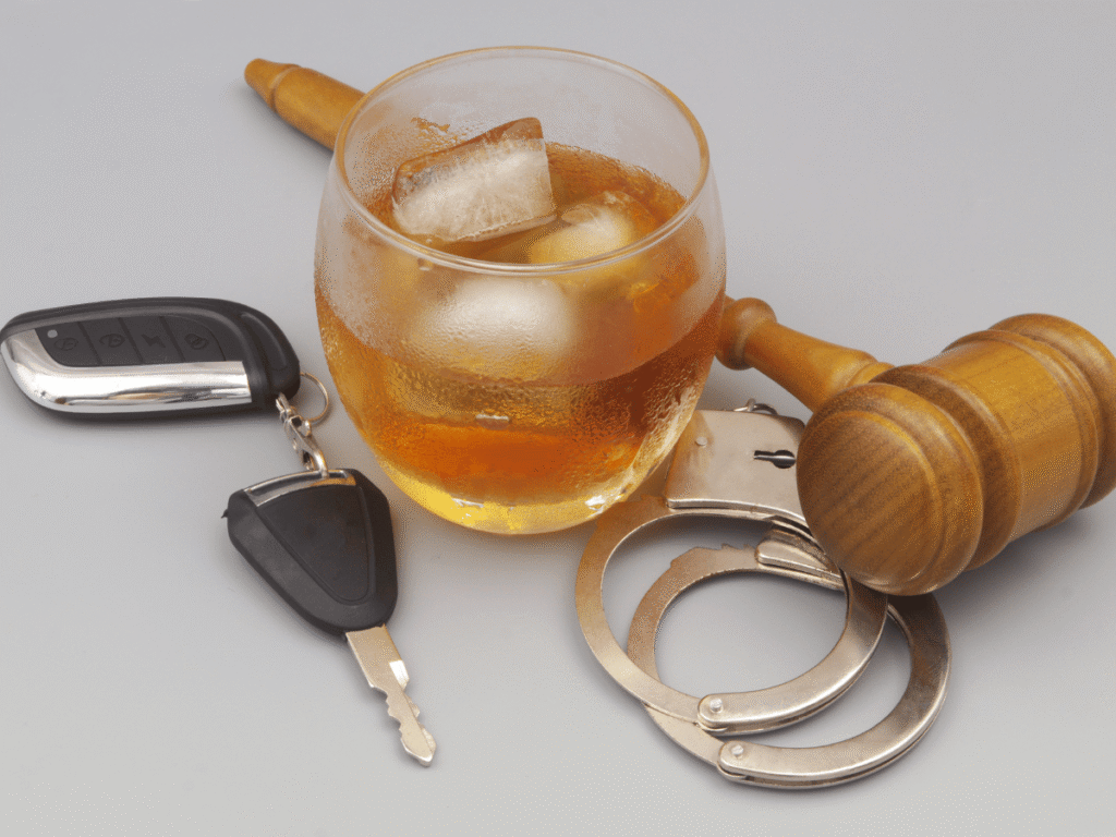 Drunk driving and court concept. Judge gavel, handcuffs, car key with glass of whisky on gray background.