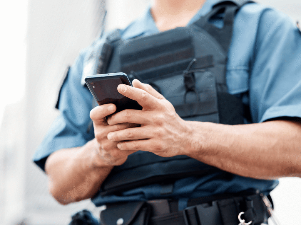 Police officer in a uniform and tactical vest operating a smartphone, illustrating the legal question of a Wyoming phone search warrant and digital privacy.