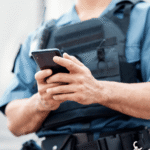 Police officer in a uniform and tactical vest operating a smartphone, illustrating the legal question of a Wyoming phone search warrant and digital privacy.