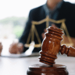 A judge's gavel resting on a block with a lawyer and scales of justice blurred in the background, symbolizing the plea bargain process Wyoming.