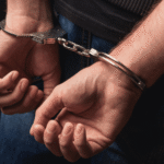 A close-up of a person’s hands cuffed behind their back, symbolizing criminal charges and prosecution without a victim pressing charges in Wyoming.