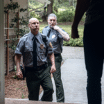 Two uniformed police officers approach the entrance of a home, viewed from the perspective of the person standing in the doorway. The officers appear serious and authoritative. The image represents questions about when Wyoming law allows police to force entry into a residence, focusing on warrants, consent, exigent circumstances, and state court rulings defining lawful entry limits.