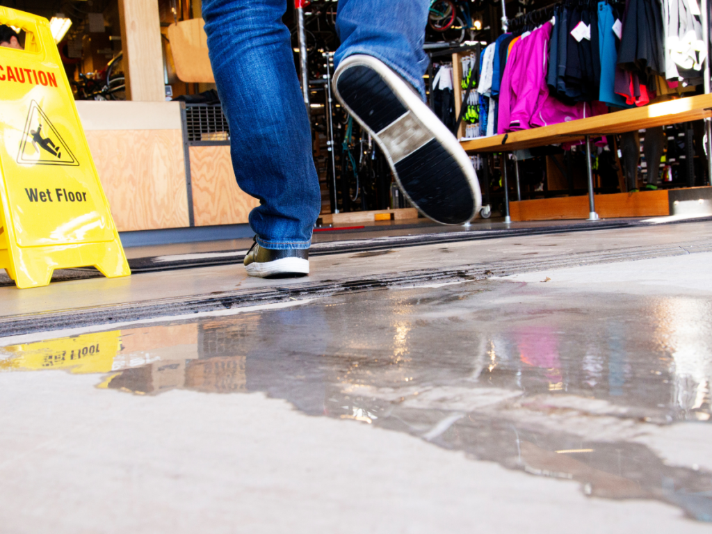 Person slipping on a wet floor inside a store near a caution sign, illustrating premises liability and the need to prove fault in a Wyoming slip and fall case.