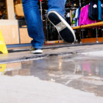 Person slipping on a wet floor inside a store near a caution sign, illustrating premises liability and the need to prove fault in a Wyoming slip and fall case.