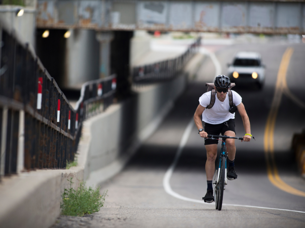 Cyclist riding on a roadway with a vehicle approaching from behind, illustrating the importance of maintaining safe passing distance under bicycle safety laws.