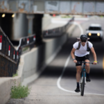 Cyclist riding on a roadway with a vehicle approaching from behind, illustrating the importance of maintaining safe passing distance under bicycle safety laws.