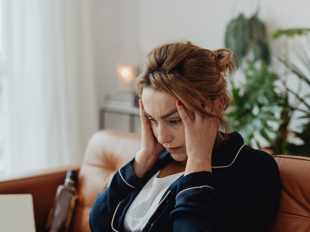 Person sitting on a couch holds their head with a distressed expression, illustrating emotional and cognitive struggles that can occur after a traumatic brain injury.