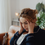 Person sitting on a couch holds their head with a distressed expression, illustrating emotional and cognitive struggles that can occur after a traumatic brain injury.