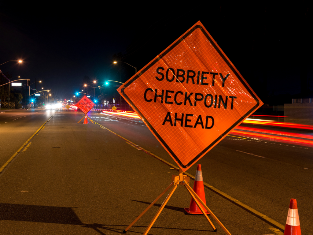 A nighttime roadside sobriety checkpoint with a visible “Sobriety Checkpoint Ahead” sign, highlighting how DUI stops are sometimes conducted in advance—and raising important legal questions about when such stops are lawful or may violate constitutional protections in Sundance, Wyoming.