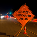 A nighttime roadside sobriety checkpoint with a visible “Sobriety Checkpoint Ahead” sign, highlighting how DUI stops are sometimes conducted in advance—and raising important legal questions about when such stops are lawful or may violate constitutional protections in Sundance, Wyoming.