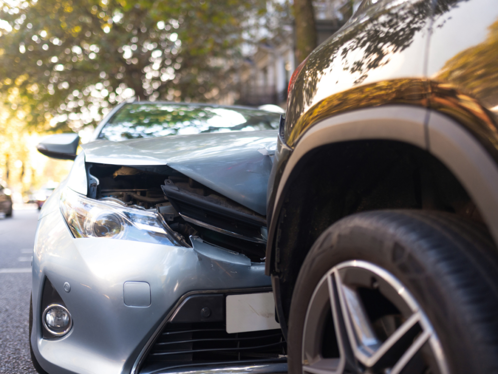 Front-end collision between a silver passenger car and the rear of a dark SUV on a residential street, showing damage to the sedan’s hood, grille, and front bumper after the crash.