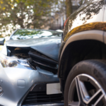 Front-end collision between a silver passenger car and the rear of a dark SUV on a residential street, showing damage to the sedan’s hood, grille, and front bumper after the crash.
