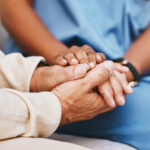 Close-up of a caregiver gently holding an elderly resident's hands, illustrating a blog about recognizing financial exploitation and protecting nursing home residents from elder financial abuse in Wyoming.